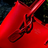 Side view of Red Italian handbag with a brand logo on a stone surface with greenery in the background. - Don de Dieu Marque