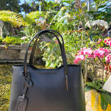 Black Italian handbag with a visible authentic brand logo in a real garden and pond setting. - Don de Dieu Marque