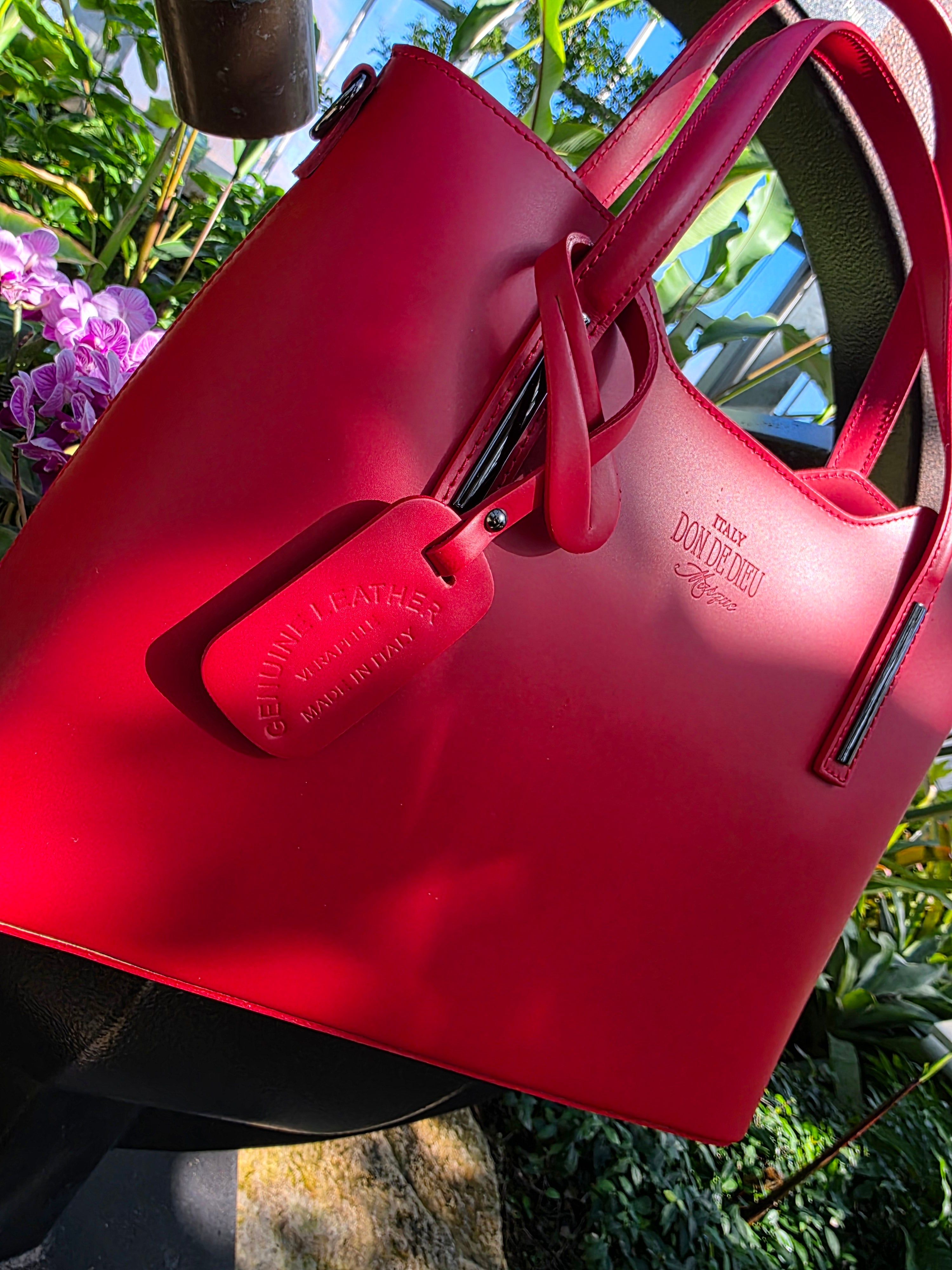 Red handbag with a visible brand logo against a natural background. - Don de Dieu Marque