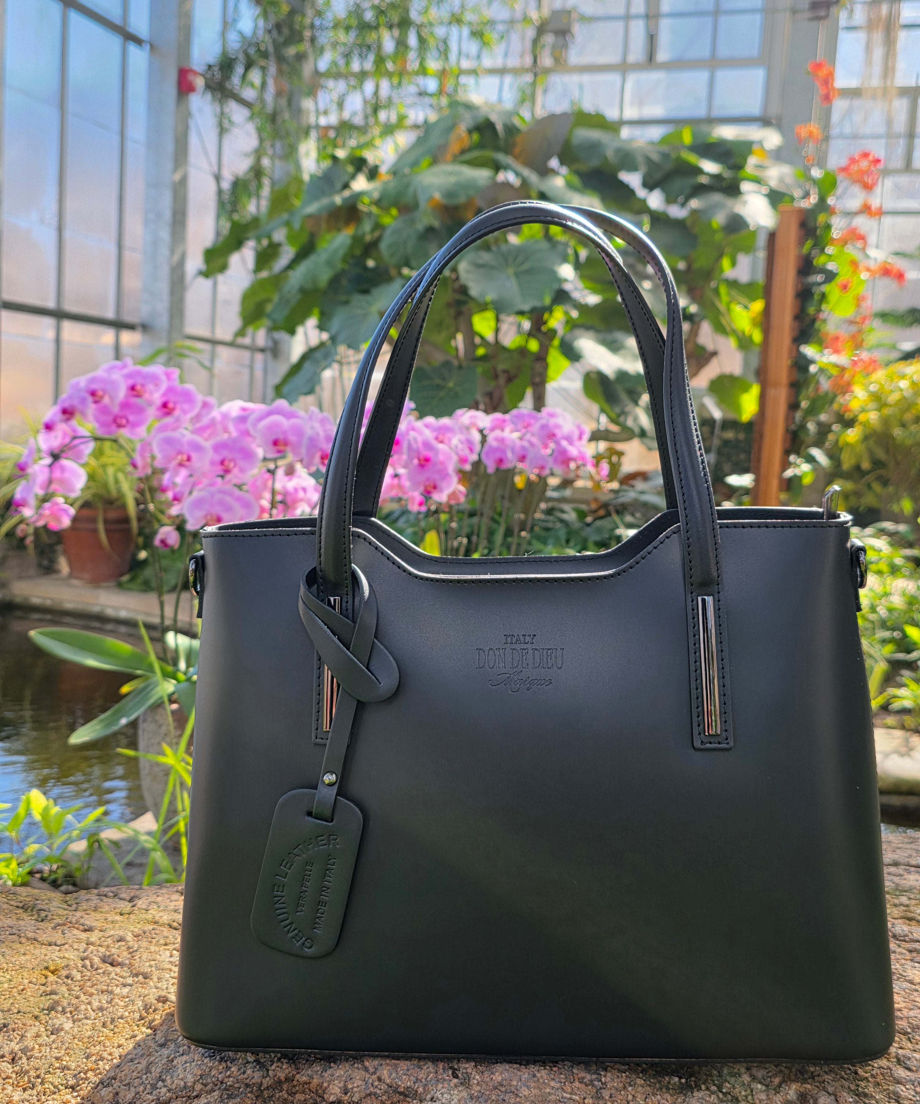 Black Italian handbag full view on a stone surface with blurred background. - Don de Dieu Marque