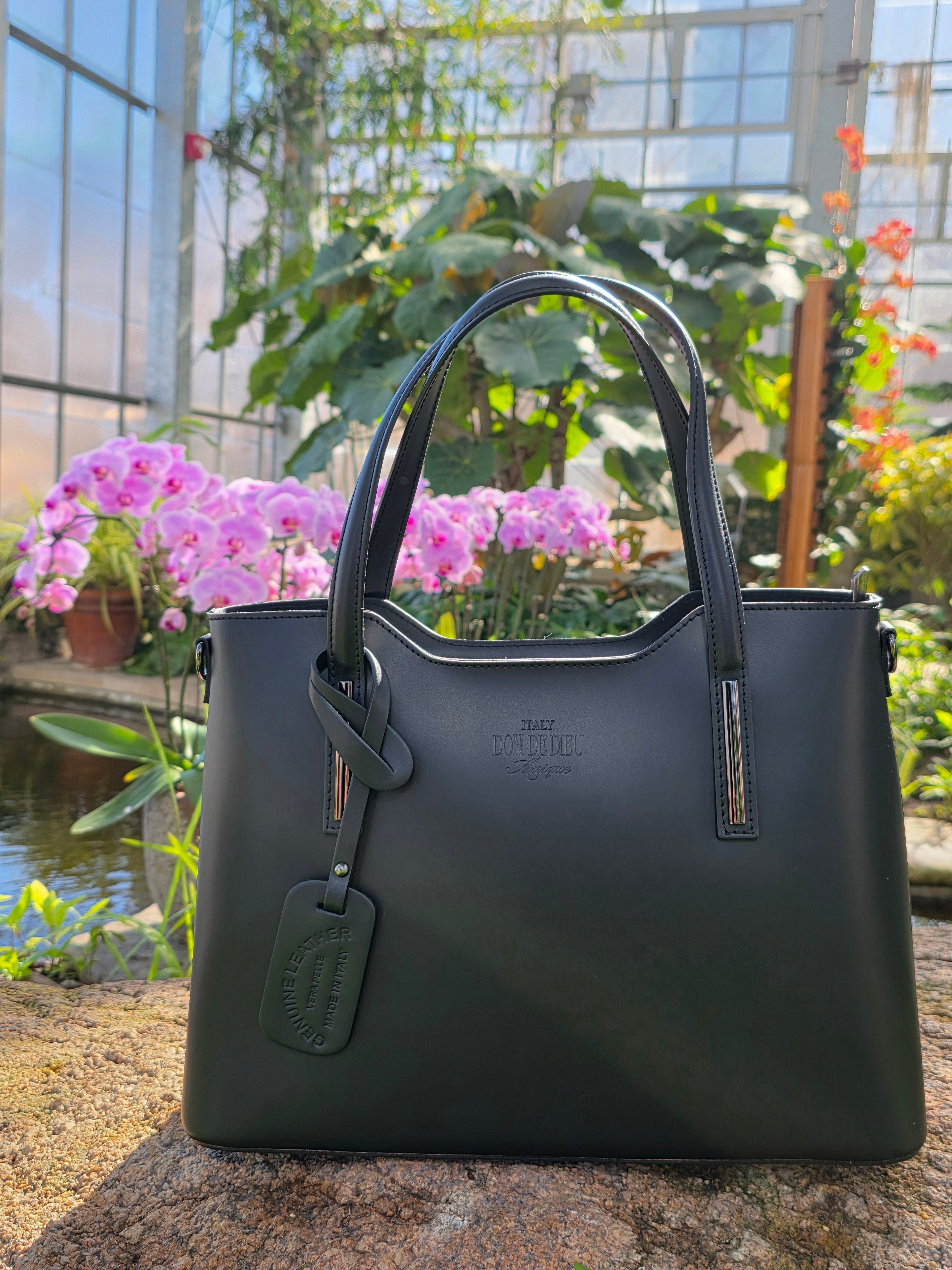 Black Italian handbag full view on a stone surface with blurred background. - Don de Dieu Marque