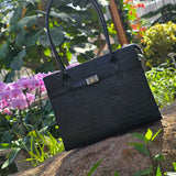 Black Croc Italian leather handbag with handle against a natural background with plants and flowers. - Don de Dieu Marque