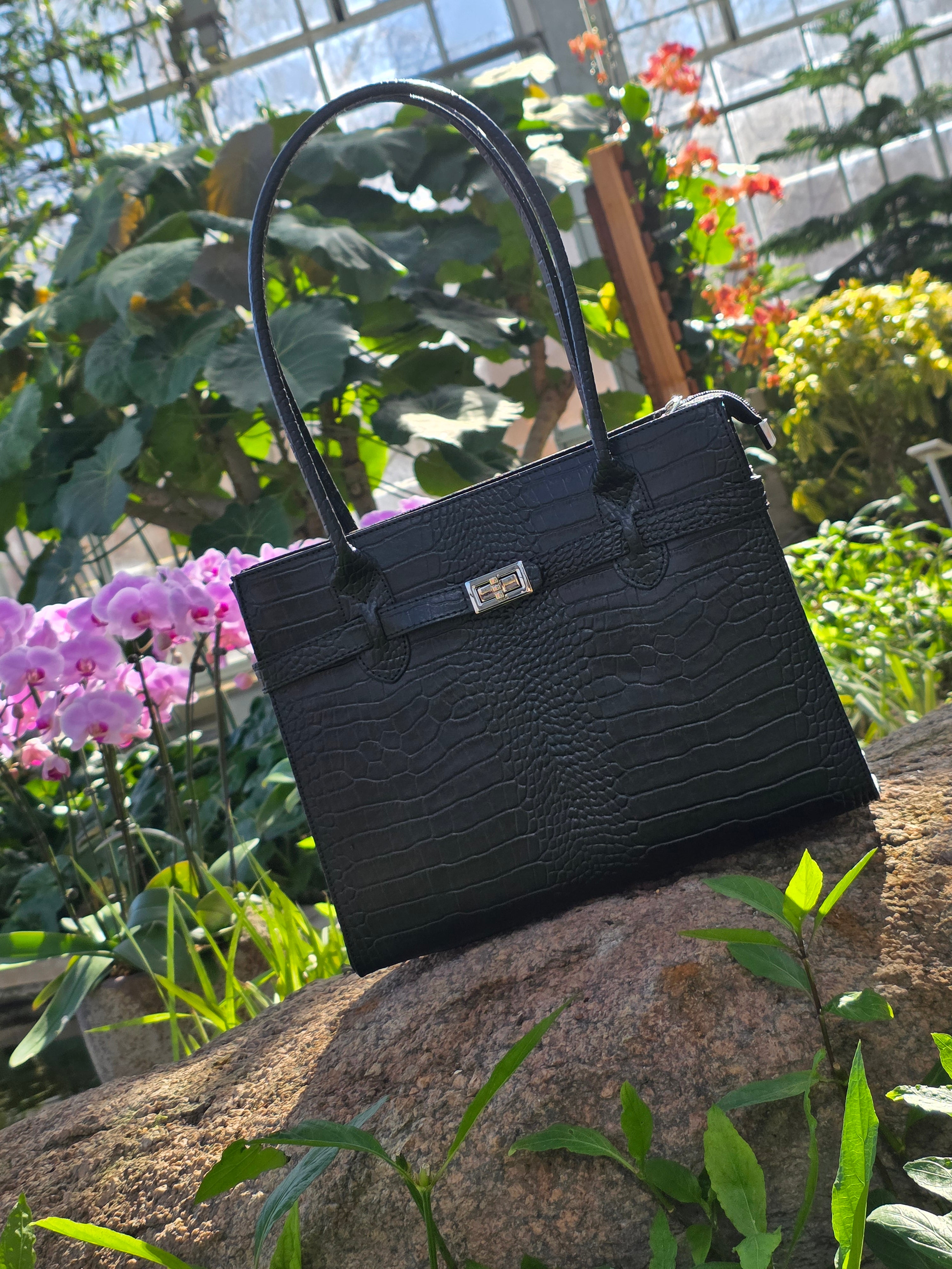 Black Croc Italian leather handbag with handle against a natural background with plants and flowers. - Don de Dieu Marque