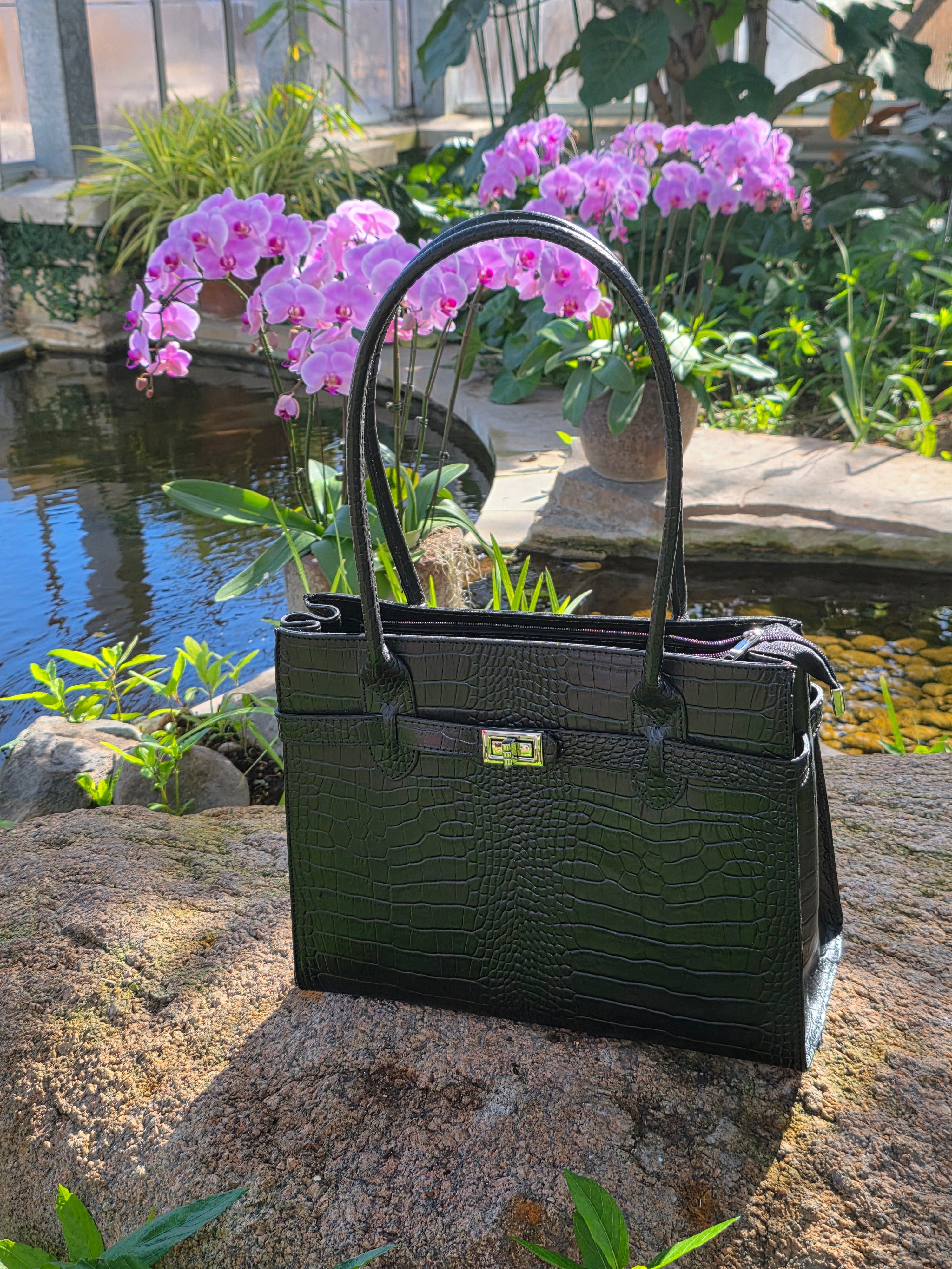 Black Italian leather full view handbag on a stone surface with pink flowers in the background - Don de Dieu Marque