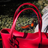 Close shot of Italian Red handbag with a visible brand logo on a rocky surface and Koi fish in background. - Don de Dieu Marque