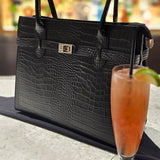 Italian Leather Black crocodile-patterned handbag styled with a glass of pink cocktail on a blurred background. - Don de Dieu Marque 