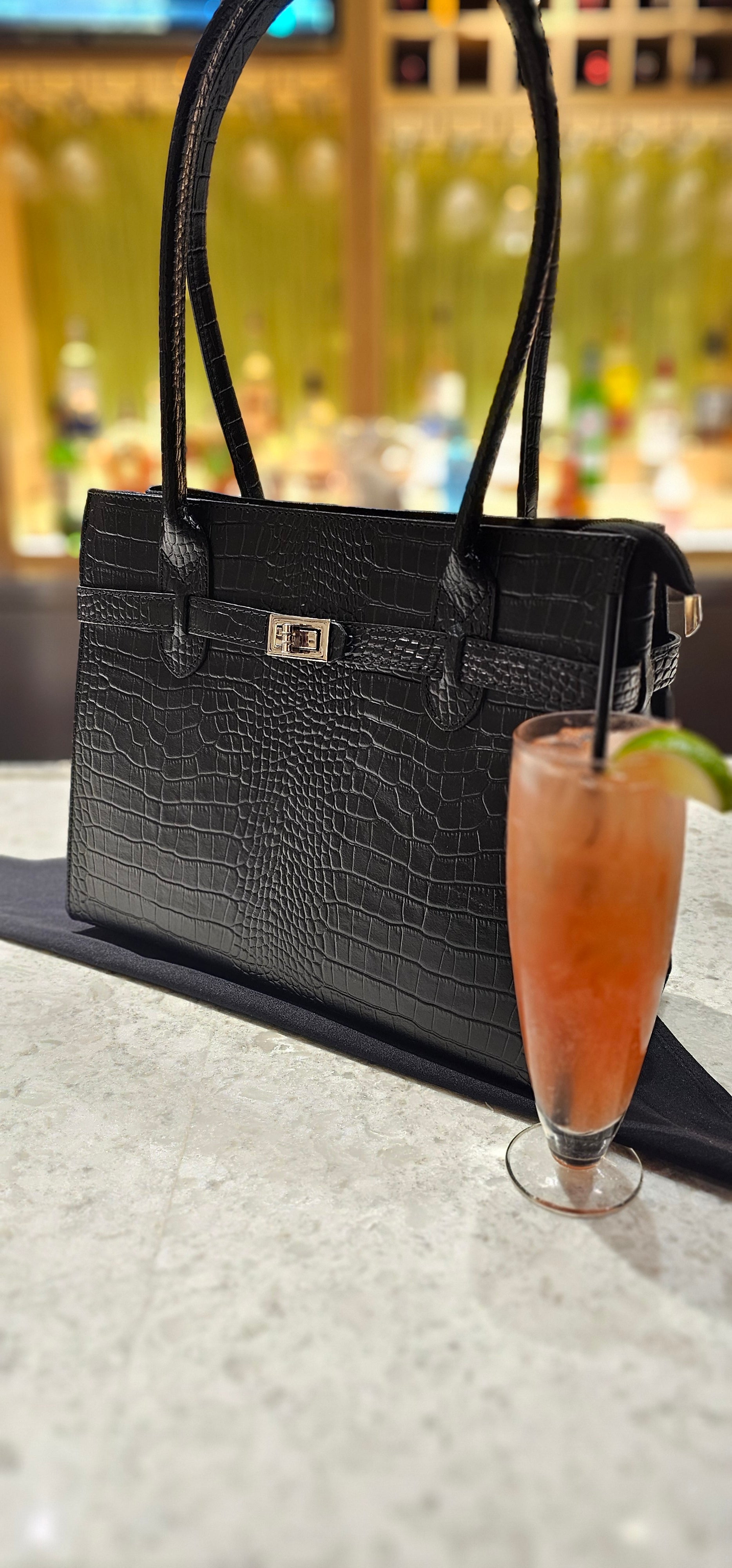 Italian Leather Black crocodile-patterned handbag styled with a glass of pink cocktail on a blurred background. - Don de Dieu Marque 