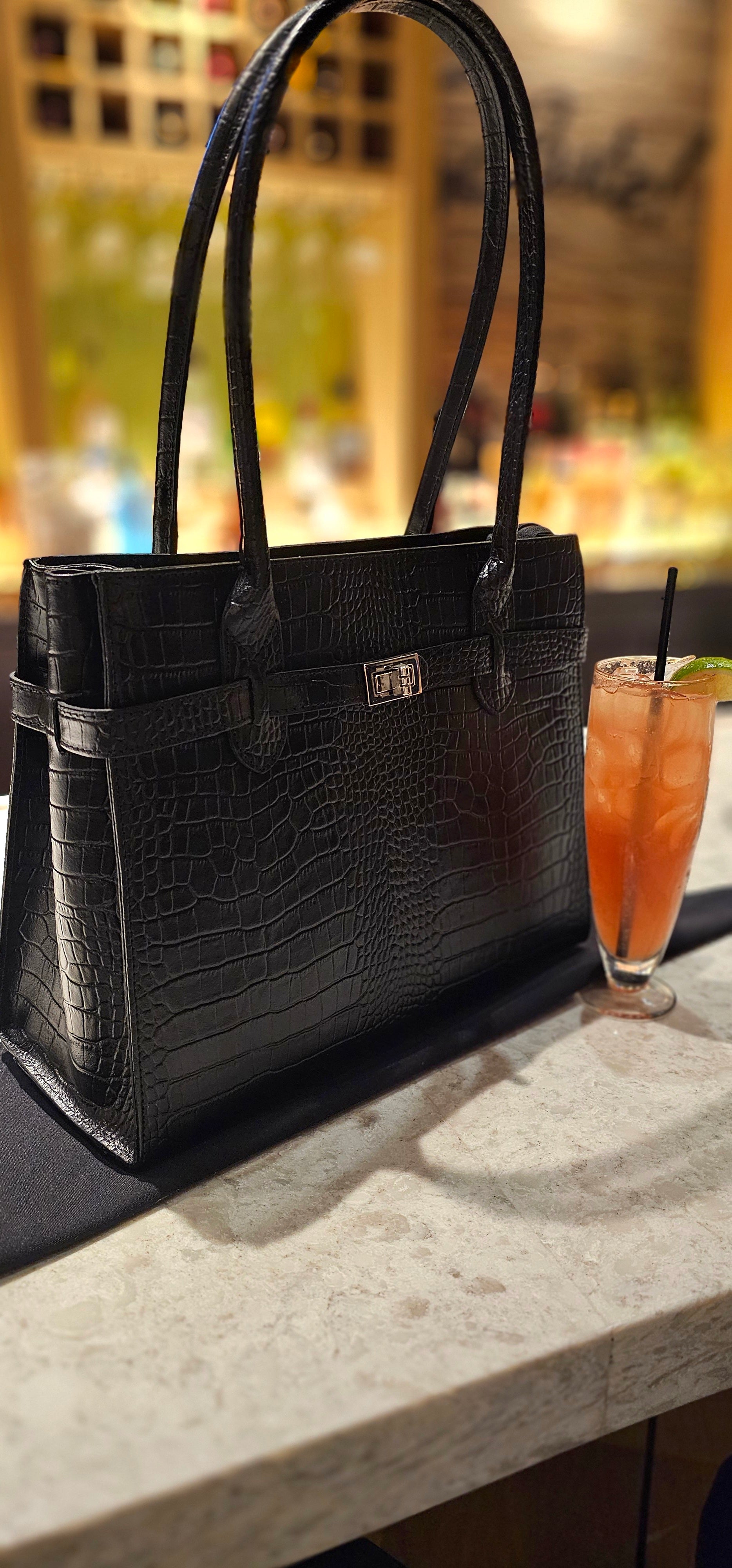 Black crocodile Italian leather handbag on a table with a blurred background. - Don de Dieu Marque