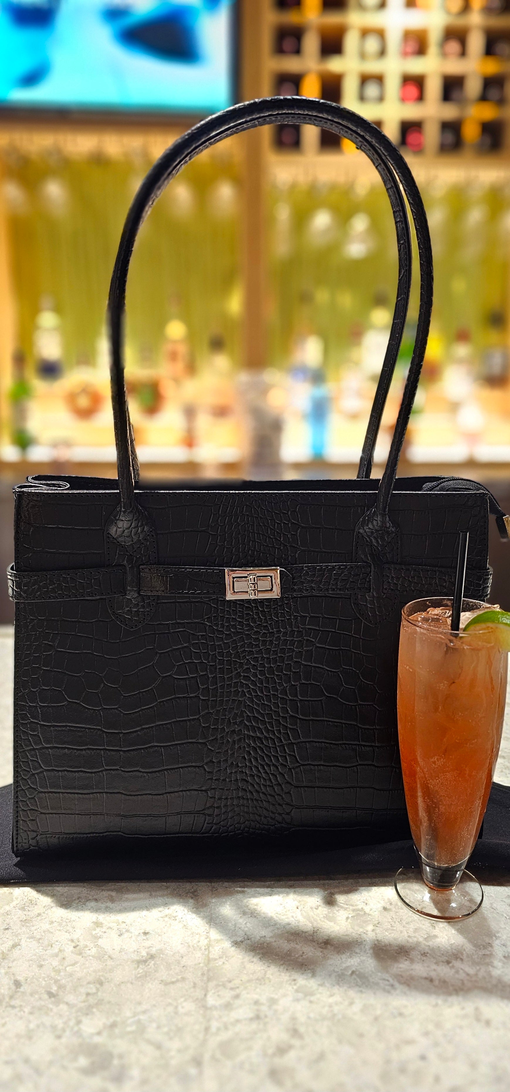 Black croc Italian leather handbag styled on a table with a cocktail in the foreground, blurred bar setting in the background. - Don de Dieu Marque