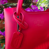 Red Italian leather handbag with visible brand logo that reads, "Italy Don de Dieu Marque" against a background of purple flowers
