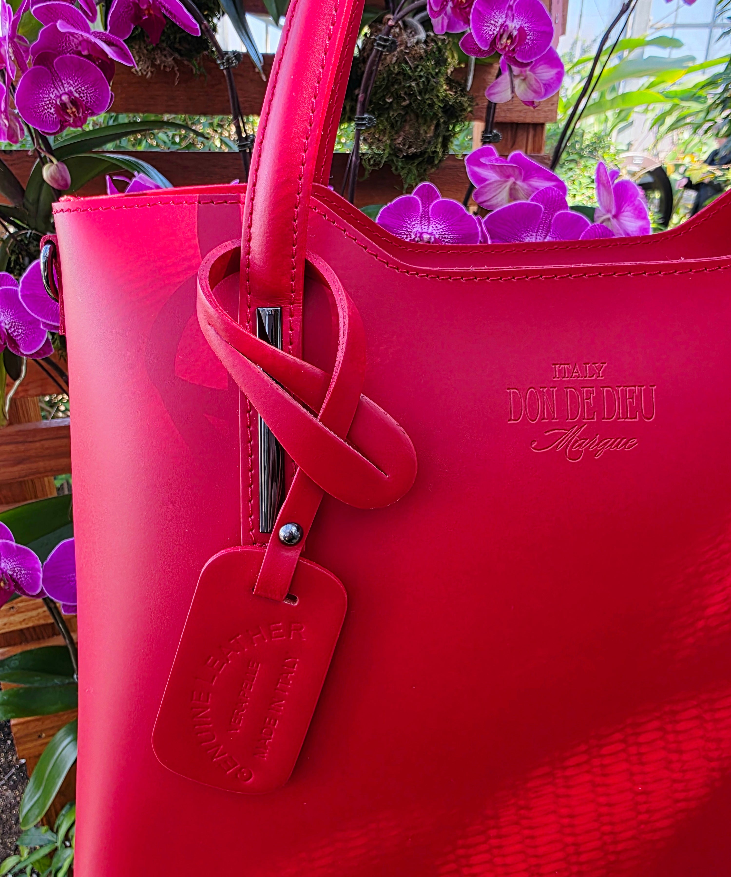 Red Italian leather handbag with visible brand logo that reads, "Italy Don de Dieu Marque" against a background of purple flowers