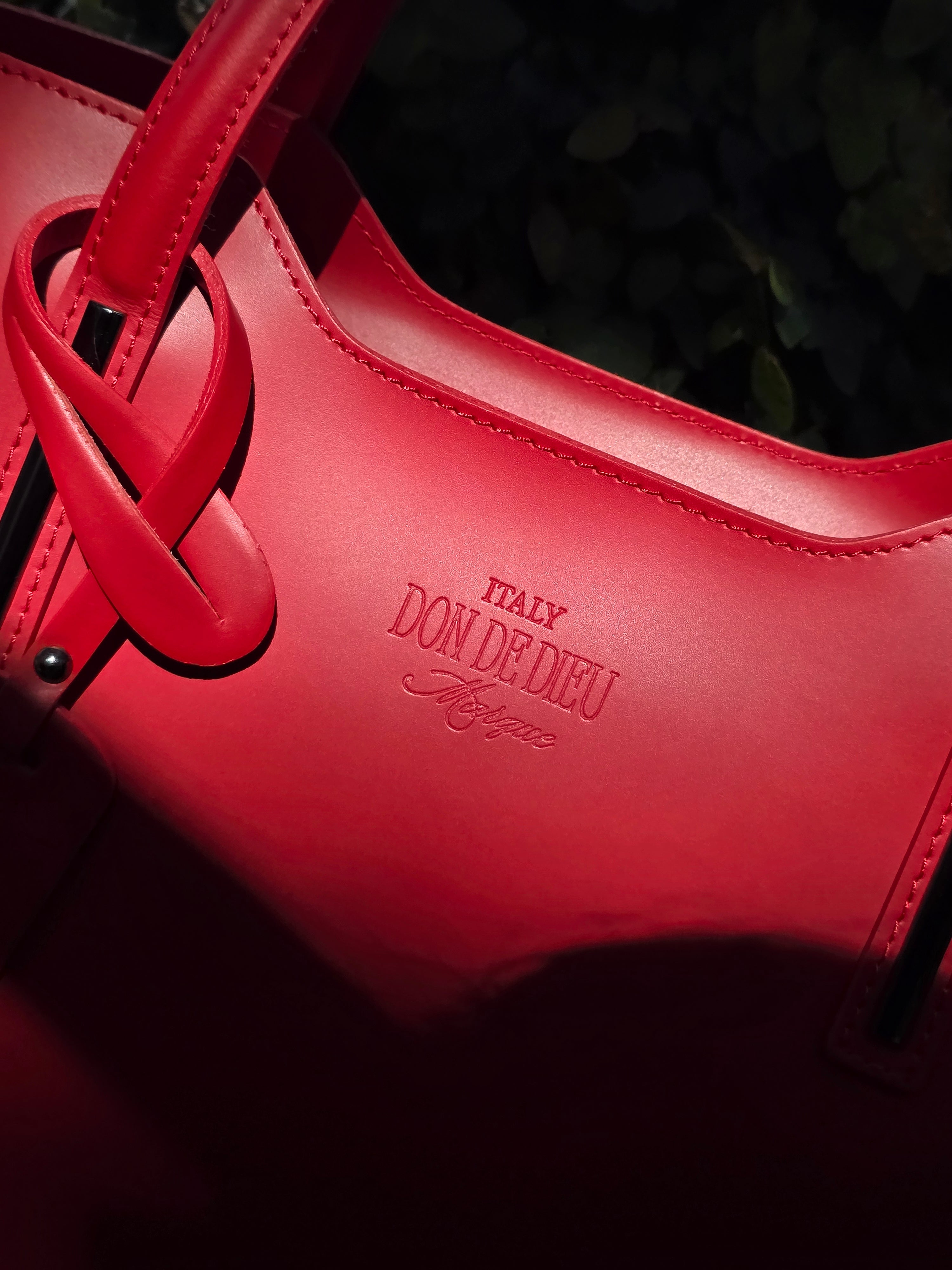 Up close detail of Red Italian leather handbag with 'Italy Don de Dieu' branding on a dark background - Don de Dieu Marque