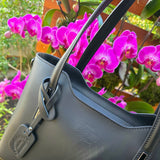 Beautiful front side of Black Italian handbag with visible brand logo in front of pink orchids. - Don de Dieu Marque