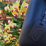 Black Italian leather bag with 'Genuine Leather Vera Pelle Made In Italy' tag in front of yellow flowers for authenticity. - Don de Dieu Marque 