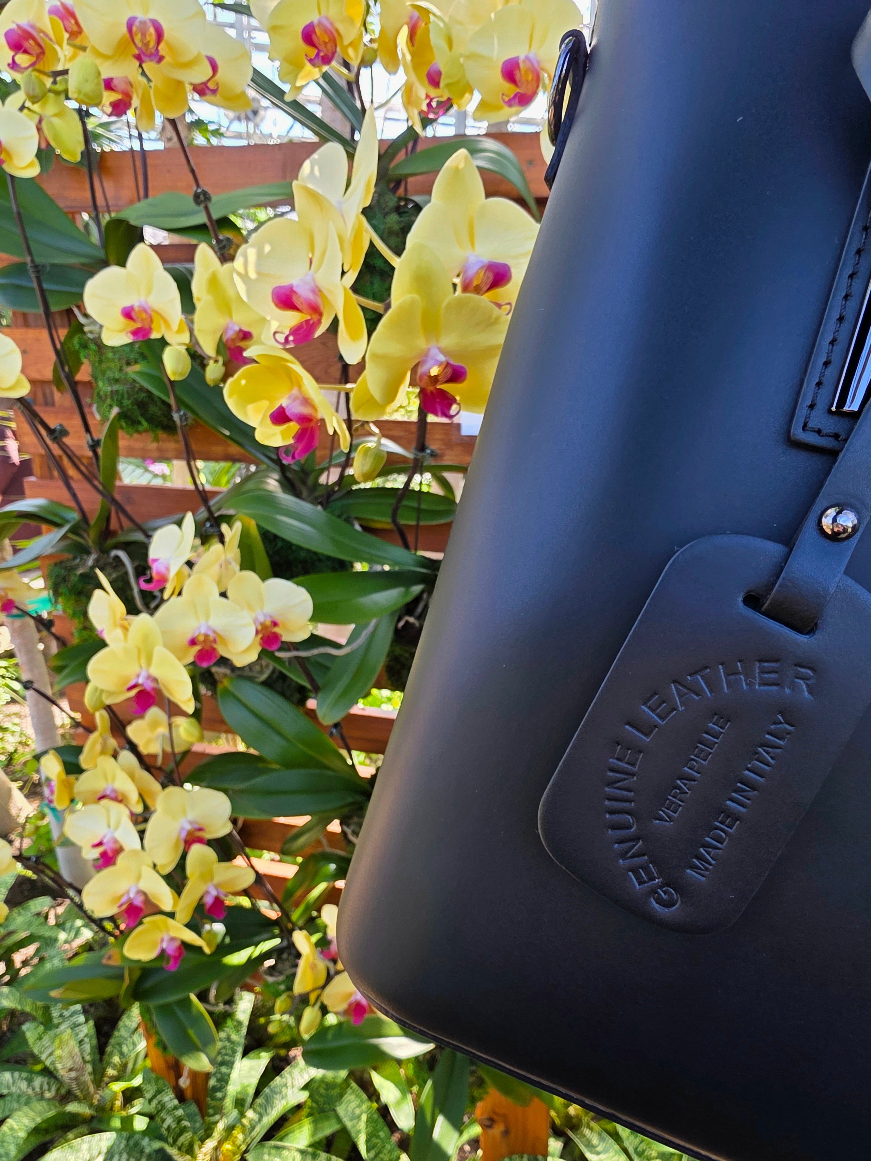 Black Italian leather bag with 'Genuine Leather Vera Pelle Made In Italy' tag in front of yellow flowers for authenticity. - Don de Dieu Marque 