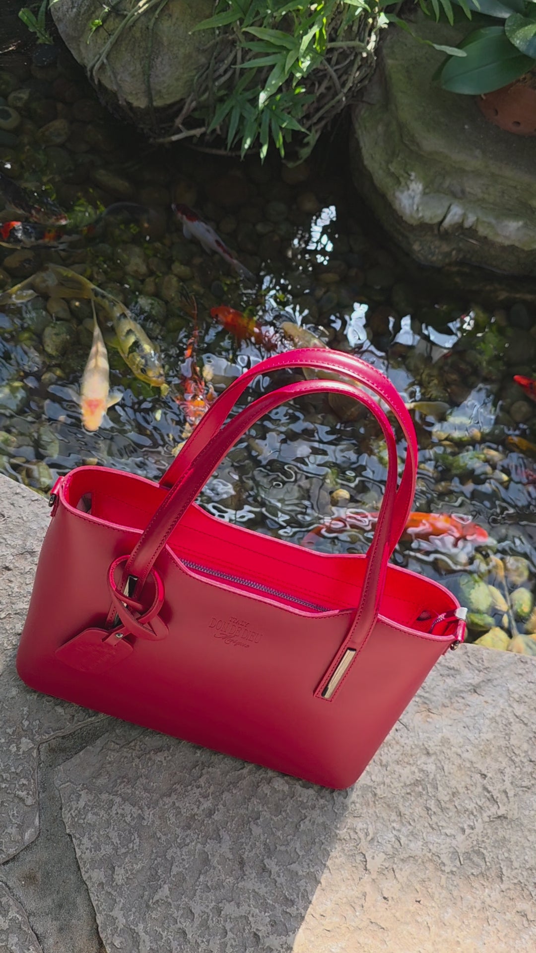 Red Italian leather handbag video view with Koi fish swimming in background pond garden. - Don de Dieu Marque